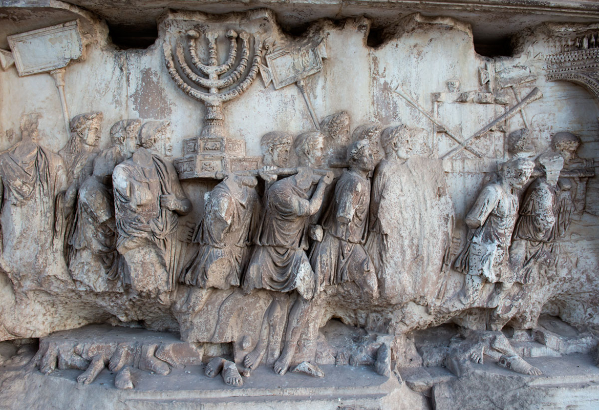 上图：提多凯旋门（Arch of Titus）上的浮雕，上面清楚描绘了第二圣殿时的金灯台和陈设饼桌子，桌上放着几个金杯，桌旁又靠着几支祭司的号筒。提多凯旋门是古罗马城遗址的一座大理石单拱凯旋门，用来纪念提多皇帝在主后70年征服和摧毁耶路撒冷。由于提多凯旋门上描绘了破坏耶路撒冷和亵渎圣殿，许多犹太人拒绝从拱门下经过，只有在1948年以色列复国时，大批人群从罗马犹太社区沿着与古罗马凯旋式相反的方向通过提多凯旋门。提多凯旋门拥有现存唯一的对第二圣殿器物的描绘。